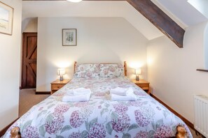A bedroom with a bed, two bedside tables, a nightstand, a wooden door, a framed picture on the wall, and a sloped ceiling. - 4 Bed in Westward Ho! (oc-n1623) (Westward Ho!)