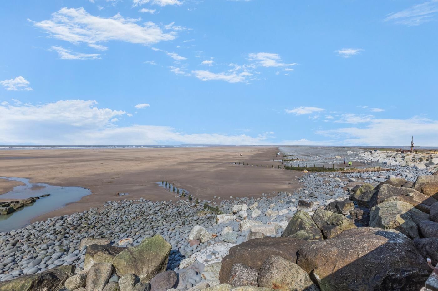 A coastal landscape with a rocky shoreline, a distant pier, and a clear sky.