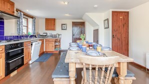 Una cucina con mobili in legno, forno integrato e tavolo da pranzo per quattro, apparecchiato con piatti bianchi e azzurri.