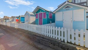 Una fila di casette colorate sulla spiaggia, con recinzioni bianche a stecche, ciascuna con un colore diverso e un piccolo portico.