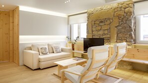 A modern living room with a stone wall, a sofa, a TV, and wooden furniture. - Santa María by FeelFree Rentals (San Sebastián)
