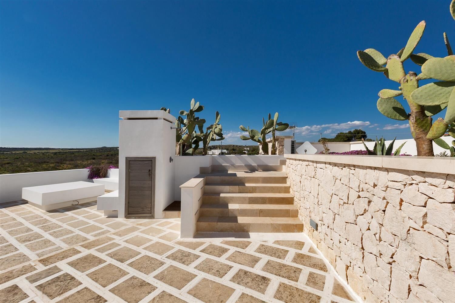 A rooftop terrace with a stone wall, a wooden door, and a staircase leading to an upper level.