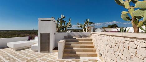 A rooftop terrace with a stone wall, a wooden door, and a staircase leading to an upper level.