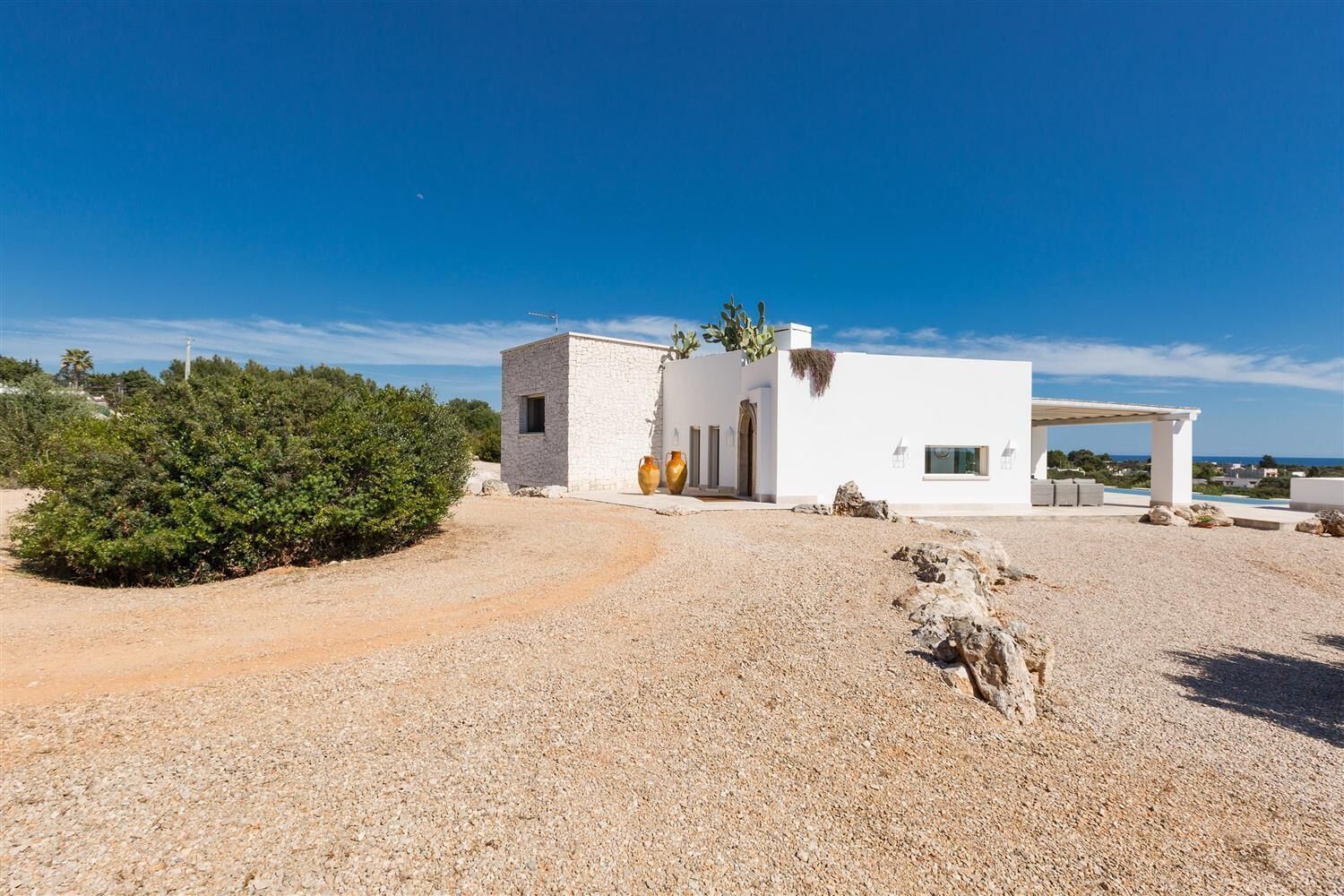 A modern white building with a gravel driveway, a covered outdoor seating area, and a view of the sea.