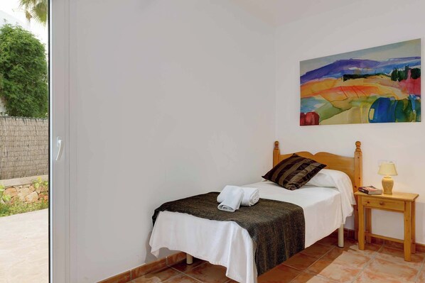 A bedroom with a bed, a nightstand, a painting, and a view of the outdoors.