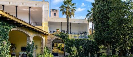 A courtyard with a covered walkway, palm trees, and a building with arches and a balcony.
