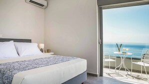 A hotel room with a bed, a balcony with a table and chairs, and a view of the sea.