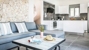 A modern living room with a grey sofa, a coffee table with magazines and a hat, and a stone wall.