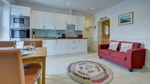 Una cocina moderna con armarios blancos, un sofá rojo y una zona de comedor con mesa y sillas.