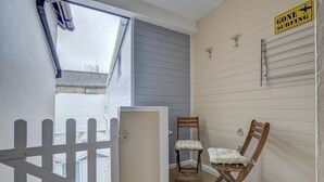 Un balcón con cerca de piquetes blancos, una silla de madera, una mesita y un cartel en la pared que dice 'GONE SURFING'.