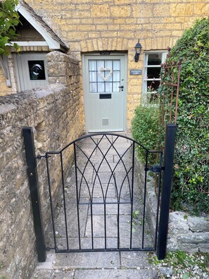 A stone wall, a metal gate, a door with a sign, and a small window. - Enchanting Grade II listed,Log Burner,allocated parking,town centre but secluded (Bourton-on-the-Water)
