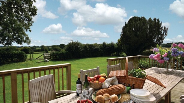 An outdoor dining area with a table set for a meal, surrounded by chairs, and overlooking a grassy landscape with trees. - Upper Mowley -  a spacious farmhouse sleeping sixteen guests (Kington)