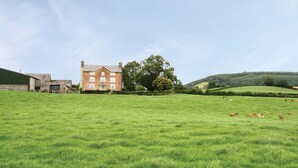 A large green field with a brick building and a barn in the background. - Upper Mowley -  a spacious farmhouse sleeping sixteen guests (Kington)