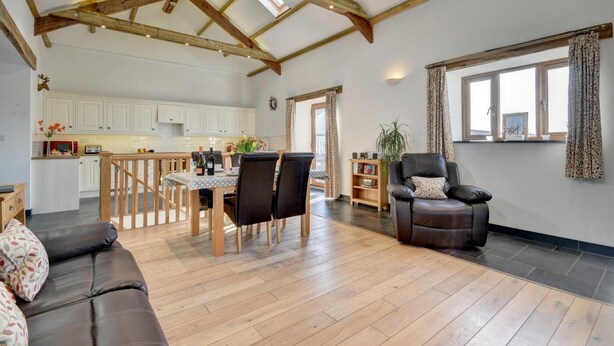 Un vaste espace de vie doté d’un plafond en bois, d’une table à manger avec des chaises, d’un canapé en cuir et d’un fauteuil en cuir noir.