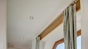 Un couloir avec une porte en bois, une grande fenêtre avec des rideaux et un sol carrelé.