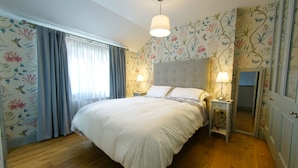 A bedroom with a large bed, two bedside tables with lamps, floral wallpaper, and a wooden floor. - Higher O'Connell 2 Kinsale, Co. Cork (Kinsale)