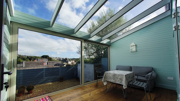 A room with a large sliding glass door leading to a balcony, a small table with a chair, and a couch. - Higher O'Connell 2 Kinsale, Co. Cork (Kinsale)