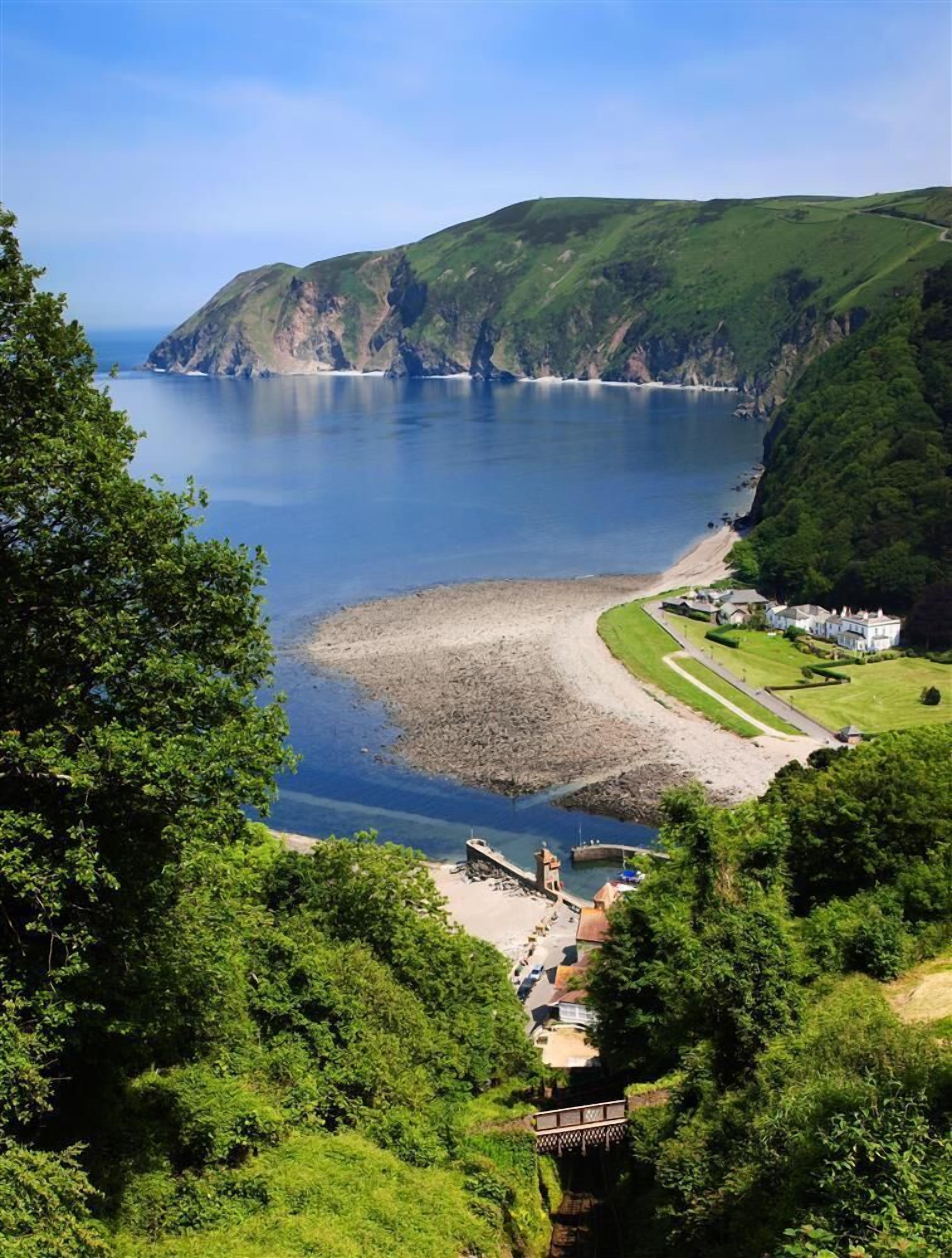 A coastal landscape with a clear view of the sea, a sandy beach, and a small building with a pathway leading to it.