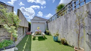 A backyard with artificial green turf, a wooden fence, a stone wall, and a wooden table with a yellow sculpture.