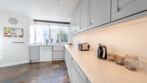 A modern kitchen with white cabinets, a stone tile floor, a toaster, a kettle, and jars on the counter.