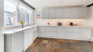 Une cuisine moderne avec des meubles blancs, une grande fenêtre et un sol carrelé en pierre.