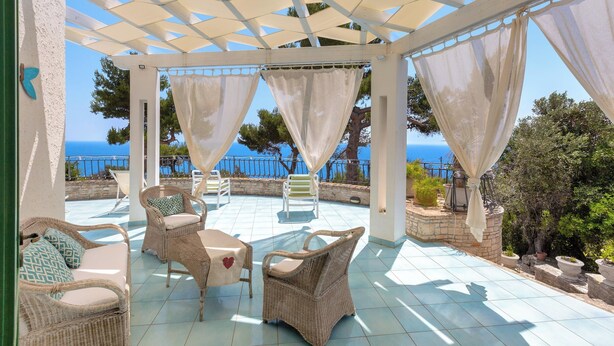 A covered patio with wicker furniture and a view of the sea.