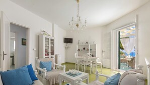 A bright living room with white furniture, a chandelier, and a view of the outside.