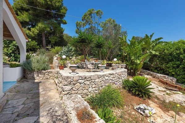 Un muro de piedra con plantas en macetas y una zona de estar con mesa y sillas.