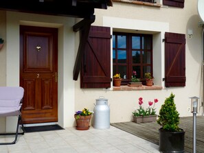 Ein Haus mit Holztür, Fensterläden, Blumentöpfen und einem kleinen Garten.