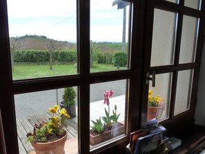 Ein Fenster mit Blick auf einen Garten und eine Straße. Auf der Fensterbank stehen Blumentöpfe und ein Schild mit der Aufschrift 'BALADES'.