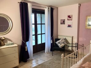 Ein Schlafzimmer mit Bett, Schminktisch, Stuhl, Glastisch und einem Fenster mit Vorhängen.