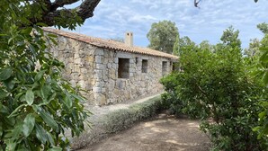 Un edificio de piedra con tejado de tejas, rodeado de follaje y un camino de grava.
