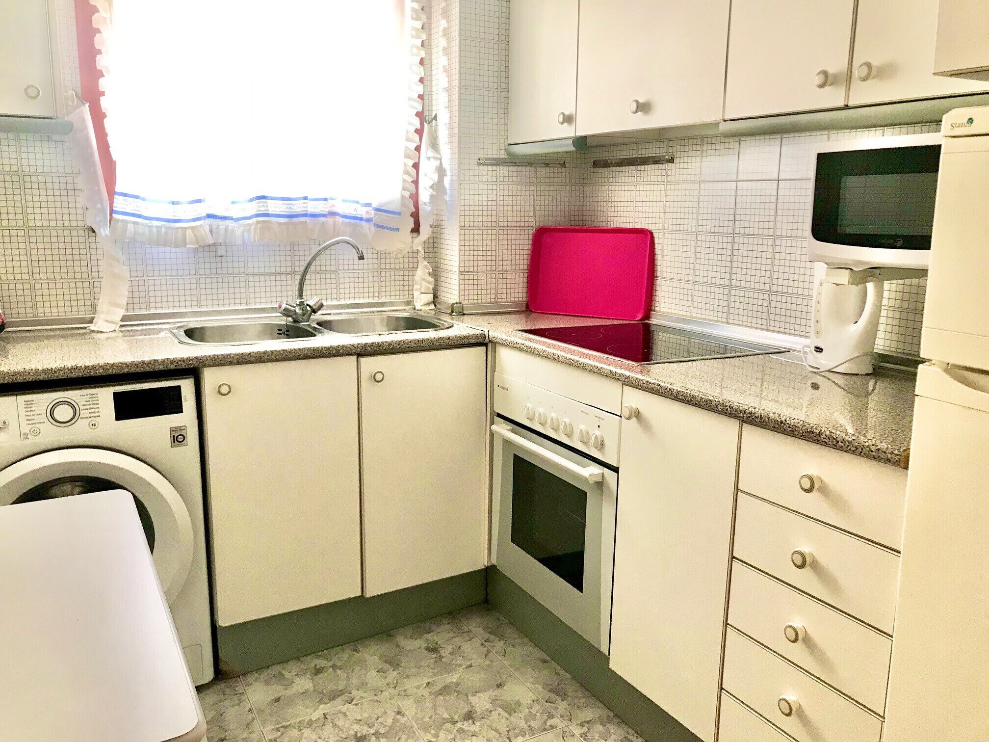 A compact kitchen with a washing machine, a microwave, and a red tray.