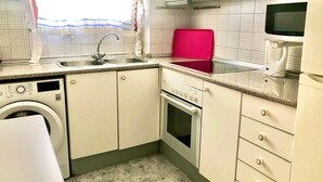A compact kitchen with a washing machine, a microwave, and a red tray. - SANTO DOMINGO APARTMENT R030 (Benidorm)