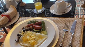 A breakfast setting with a plate of eggs, sausages, and vegetables, a glass of orange juice, and a vase with flowers. - A REAL HOME AWAY FROM HOME EXPERIENCE.... (Cape Town)