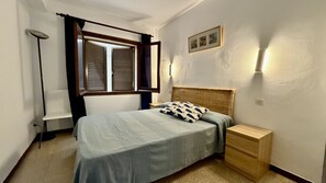Quarto com cama, mesa de cabeceira, luminária e janela com persianas.