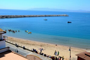 A beach with a rocky breakwater, a clear blue sea, and a few boats.
