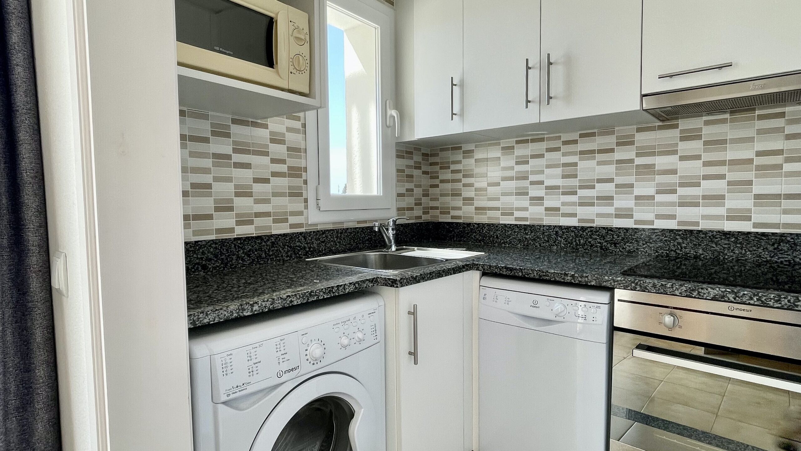 A compact kitchen with a washing machine, a microwave, and a built-in oven.