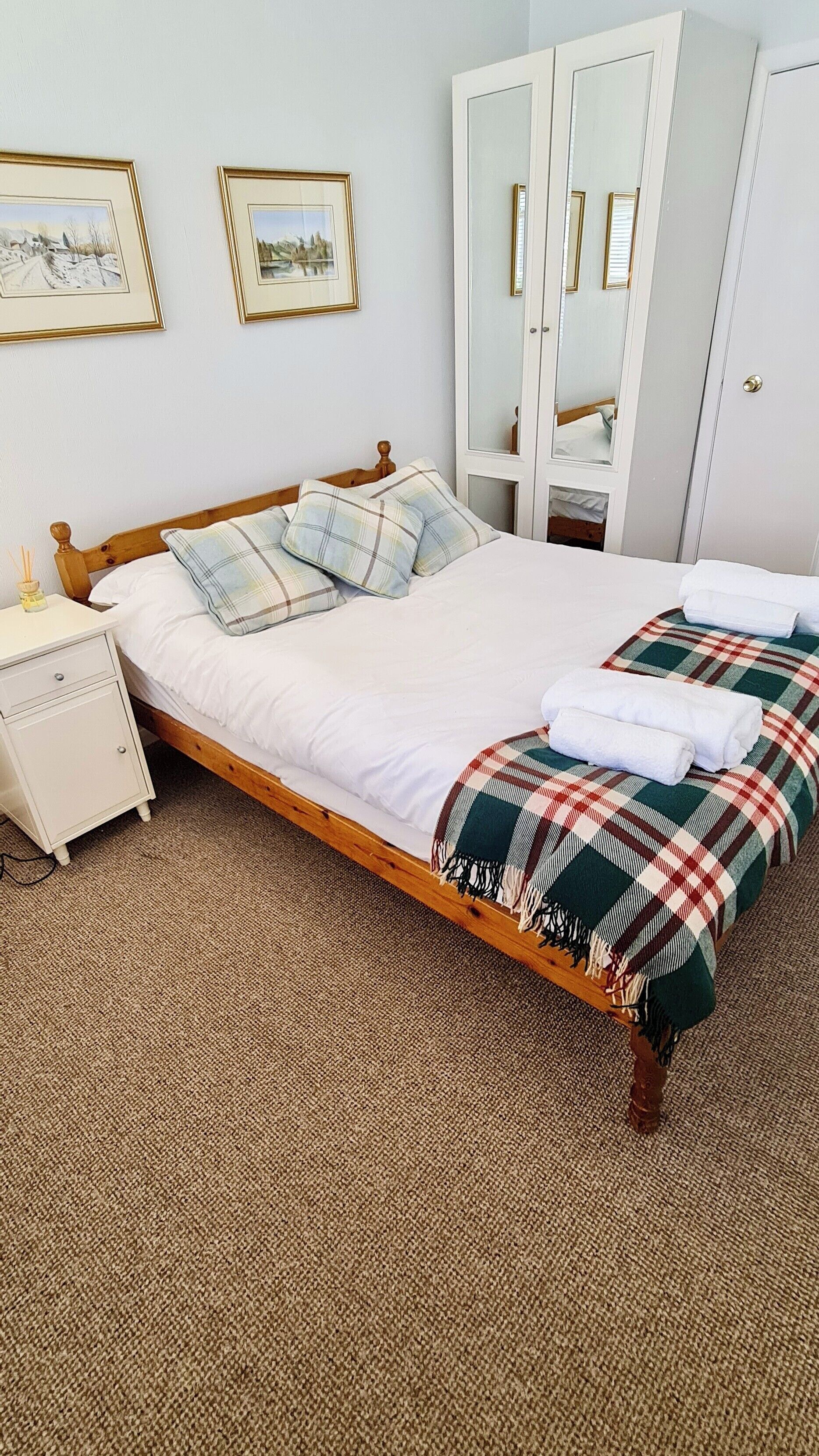 A neatly made bed with a plaid blanket, a bedside table with a lamp, and a wardrobe with mirrors.