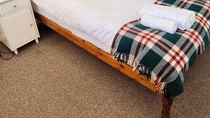 Una cama bien hecha con una manta escocesa, una mesita de noche con una lámpara y un armario con espejos.