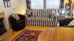 Una sala de estar con sofá, mesa de comedor, chimenea y ventana con cortinas.
