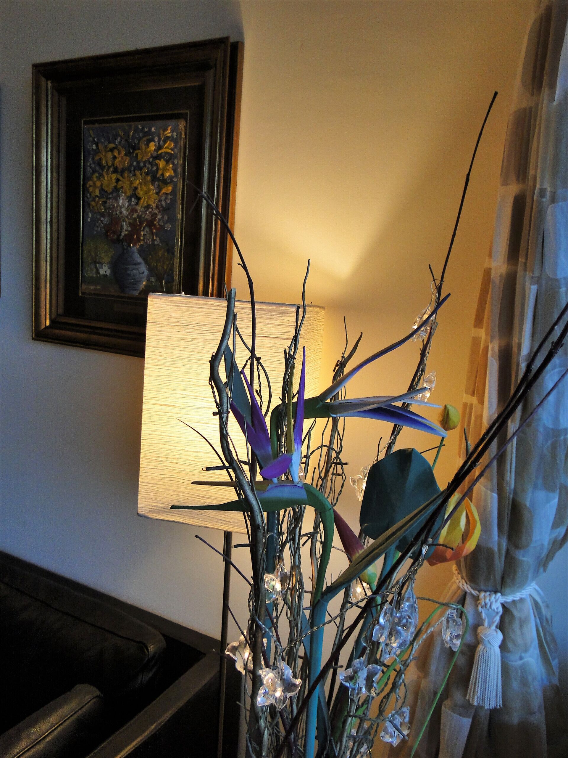 A room with a lamp, a framed picture on the wall, and a plant in a vase.