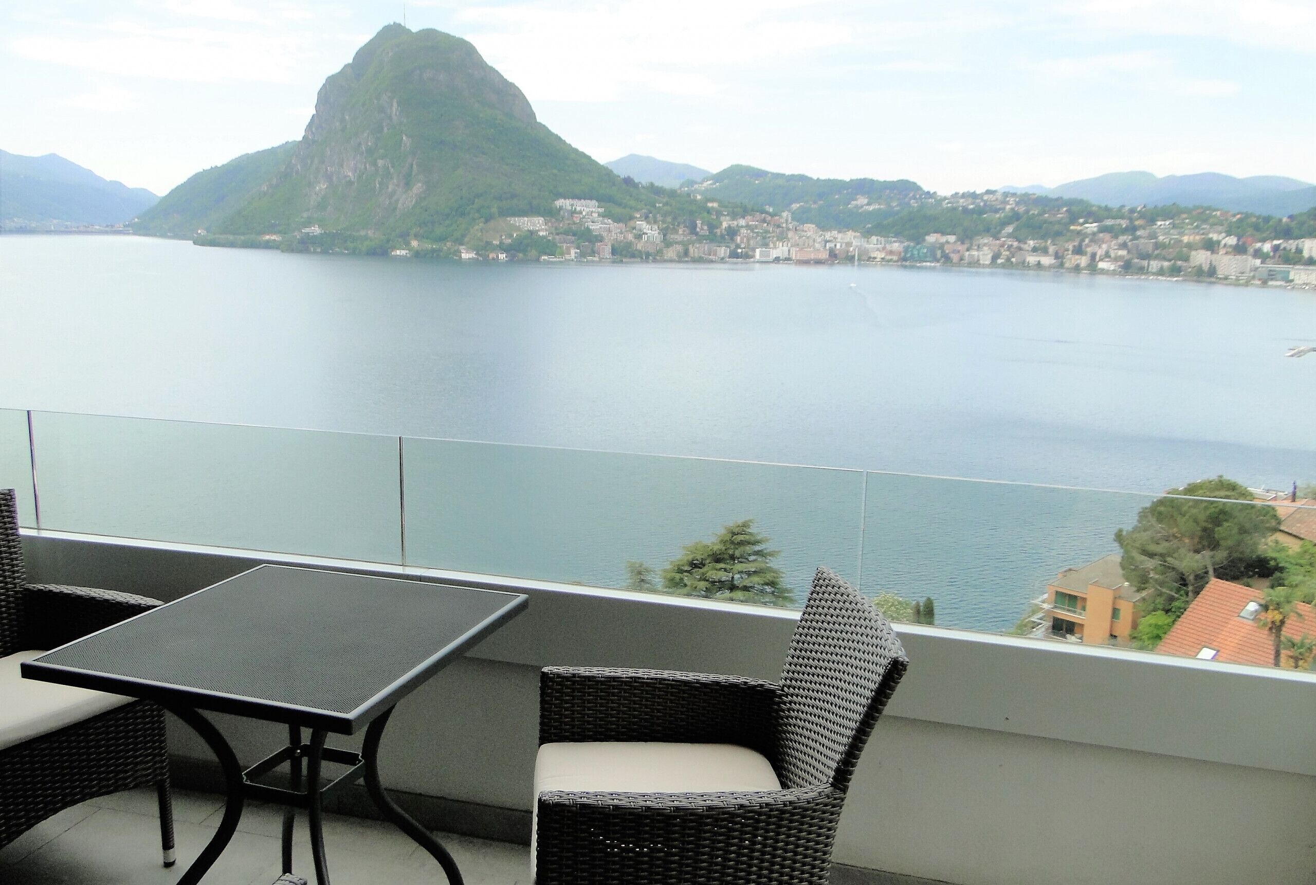 Ein Balkon mit Tisch und Stühlen, mit Blick auf einen See und Berge.