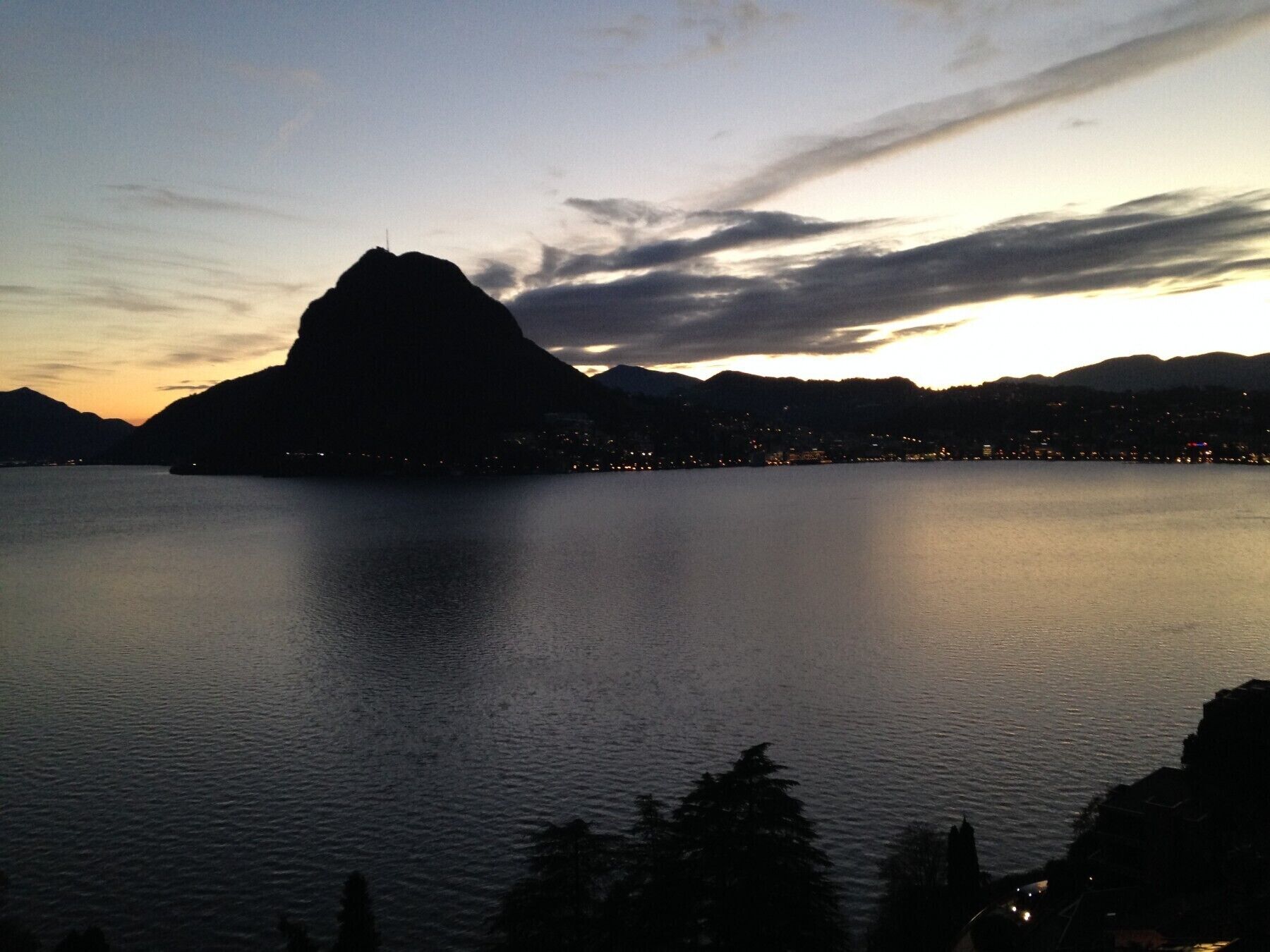 A mountain silhouette at dusk with a calm lake in the foreground.