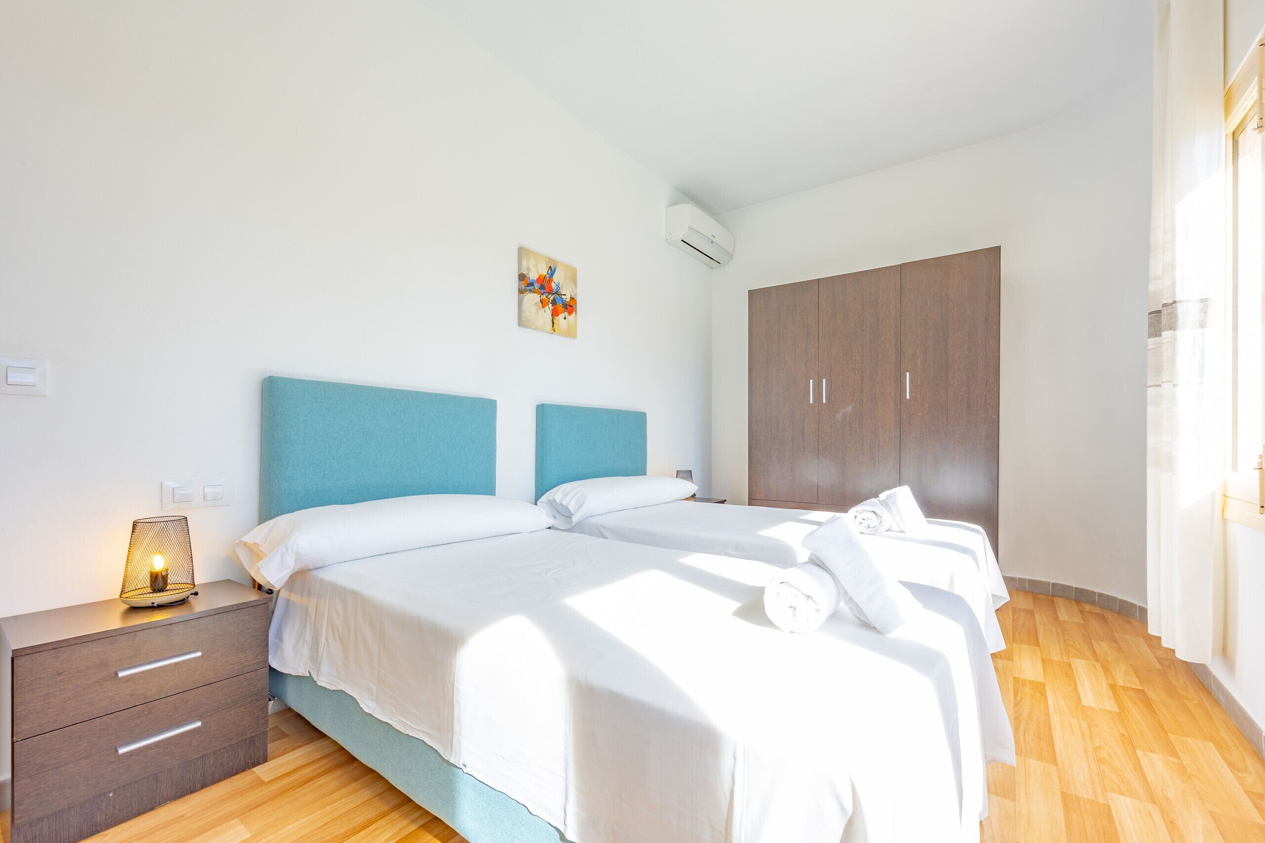 Un dormitorio con dos camas, una mesita de noche con lámpara, un armario y un cuadro en la pared.