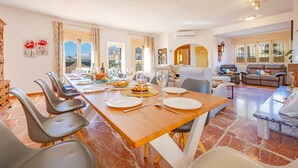 Un espace repas avec une longue table dressée pour six personnes, entourée de chaises modernes, et un coin salon avec des canapés et une table basse.