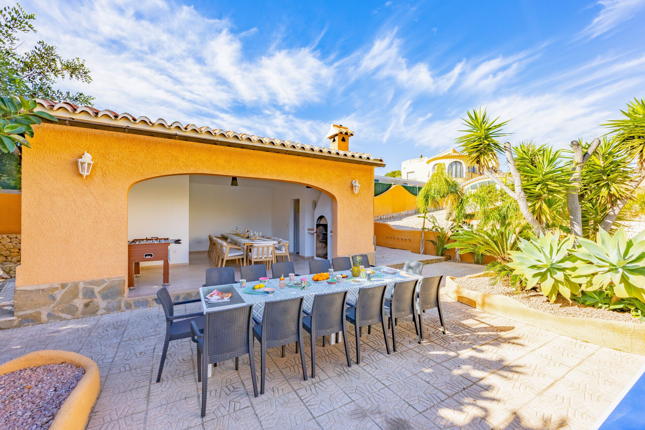 Un patio al aire libre con una mesa de comedor dispuesta para seis personas, rodeada de sillas y una mesa de billar al fondo.