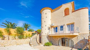 Une villa de style méditerranéen, dotée d’une façade en pierre, d’une tourelle et d’un balcon orné d’une rambarde en métal.
