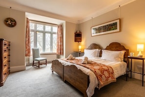 Une chambre avec un grand lit, une chaise, une commode et une fenêtre avec des rideaux.