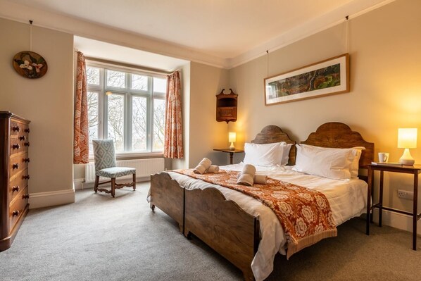 Une chambre avec un grand lit, une chaise, une commode et une fenêtre avec des rideaux.